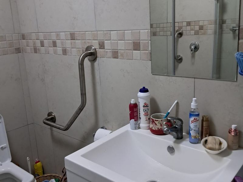 A functional bathroom featuring a vanity cabinet with basin, wall-mounted grab rail, and tiled wall finishes.