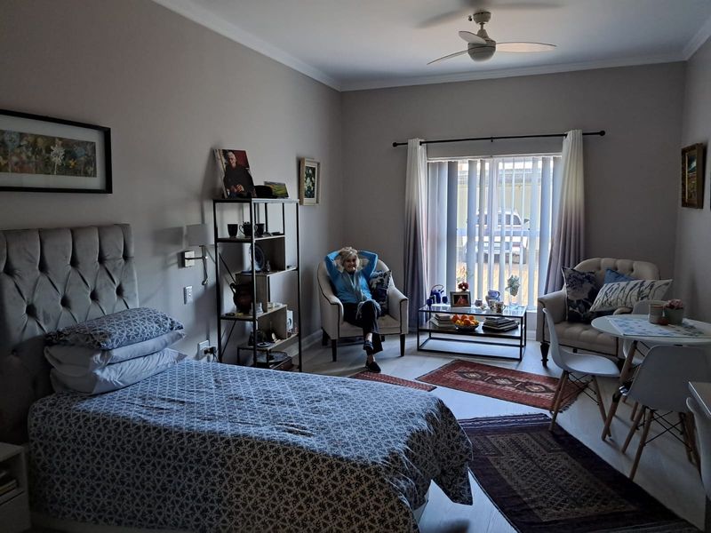 A well-maintained bedroom featuring a ceiling fan, neutral wall tones, and large windows with vertical blinds allowing for natural light.
