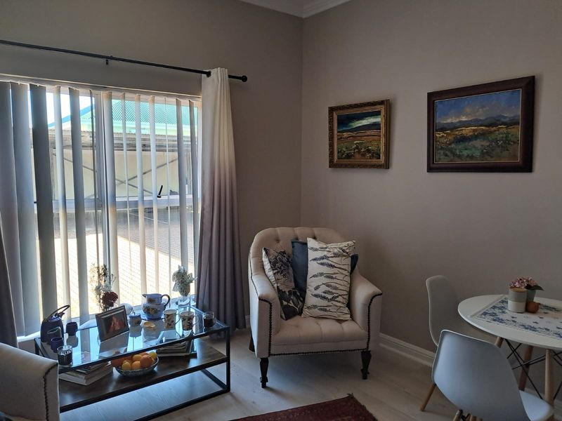 A well-maintained living area featuring laminate flooring, neutral wall tones, and large windows with vertical blinds, providing a bright and comfortable space.