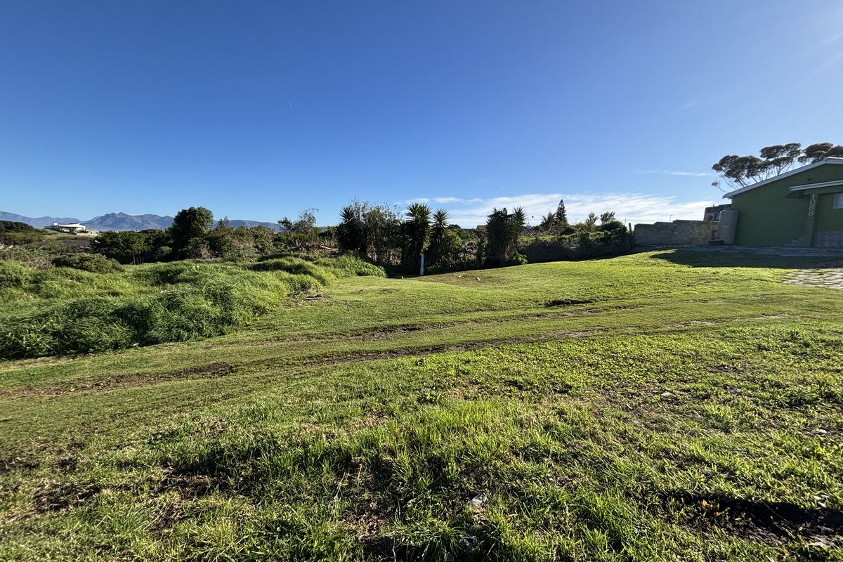 A view of a vacant residential plot featuring a grass lawn and boundary wall, with mountain views in the distance.