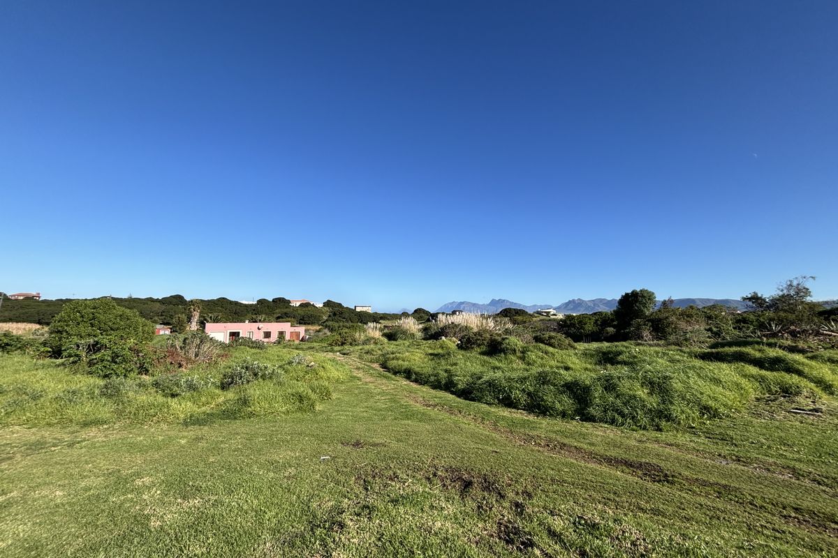 A wide-angle view of a vacant residential plot featuring natural grassland and surrounding landscape with distant mountain views.