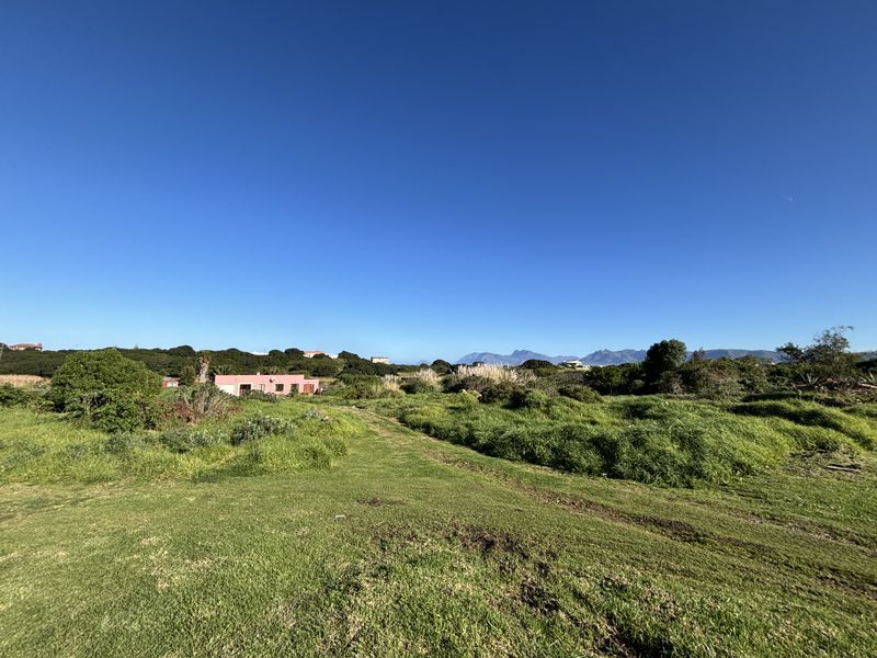 A wide-angle view of a vacant residential plot featuring natural grassland and surrounding landscape with distant mountain views.