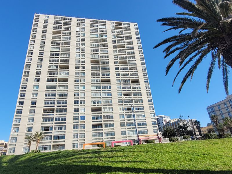 A low-angle view of a high-rise apartment building featuring multiple levels of balconies and a concrete exterior facade.