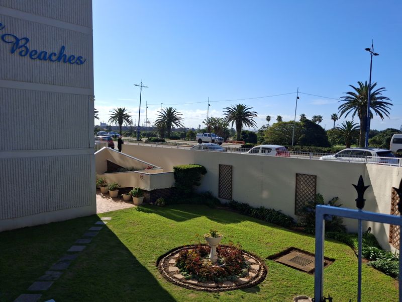 A well-maintained front garden area featuring a landscaped circular garden bed, paved pathways, and a boundary wall adjacent to the apartment building.