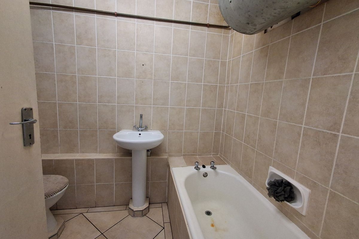 A dated bathroom featuring a pedestal basin, bathtub, and full-height wall tiling, requiring modernization of fixtures and finishes.