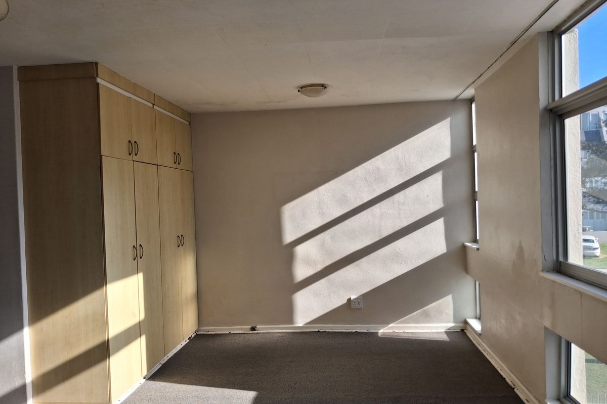 An empty bedroom featuring built-in cupboards, carpeted flooring, and large windows that provide natural light.