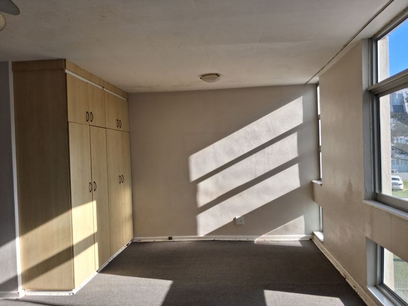 An empty bedroom featuring built-in cupboards, carpeted flooring, and large windows that provide natural light.