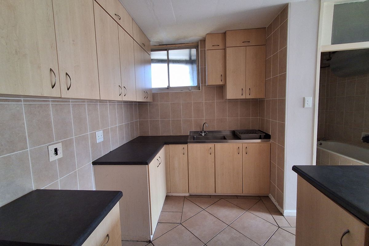 A dated kitchen featuring laminate cabinetry, dark countertops, and ceramic tiling, currently vacant and in need of cosmetic updates.