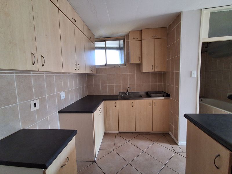 A dated kitchen featuring laminate cabinetry, dark countertops, and ceramic tiling, currently vacant and in need of cosmetic updates.