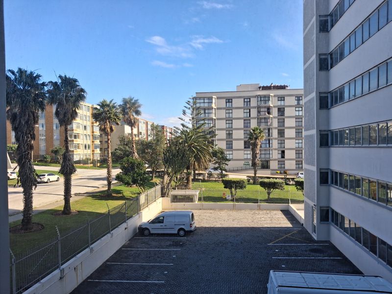 An elevated view overlooking a paved parking area, surrounding apartment buildings, and landscaped grounds within the residential complex.