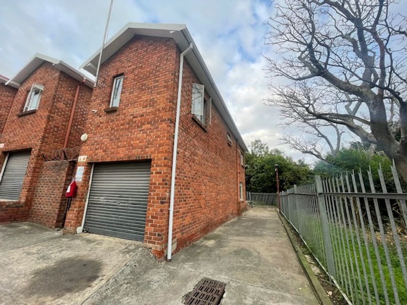 Exterior view of a face brick townhouse featuring a roller shutter garage door, concrete driveway, and perimeter metal security fencing.