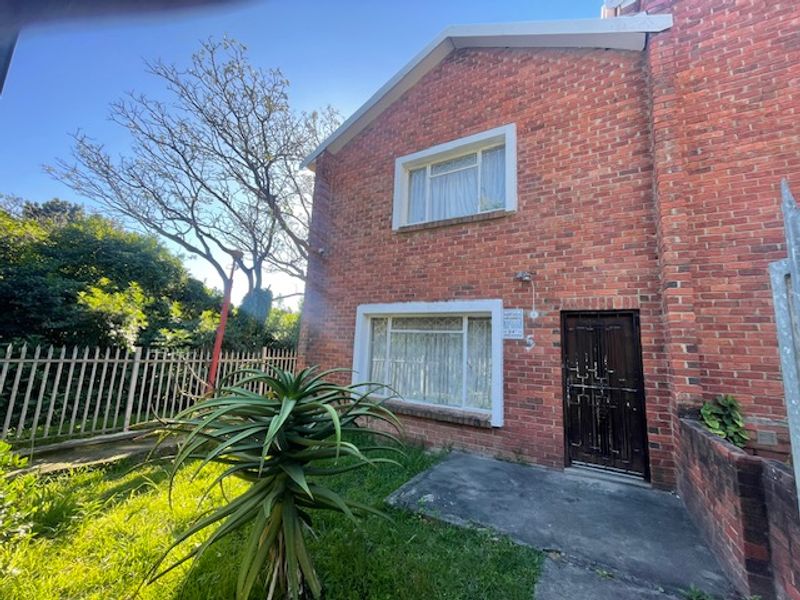 Front elevation of a double-story face brick townhouse featuring a secure entrance gate, concrete pathway, and established garden area.