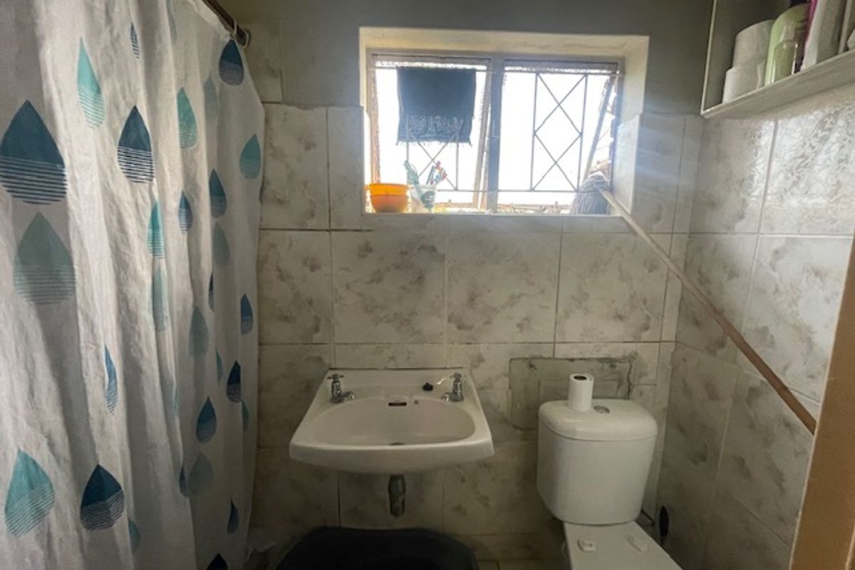 Compact bathroom featuring a wall-mounted basin, toilet, and tiled finishes. The space requires cosmetic updates and repairs to the wall tiling.