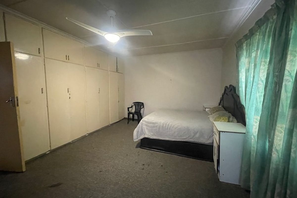 Spacious bedroom featuring extensive built-in cupboards and a ceiling fan, offering a functional layout with potential for cosmetic updates.