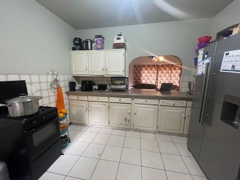 A functional kitchen featuring tiled flooring, a tiled splashback, and built-in cabinetry with a laminate countertop, connected to the living area via an archway.