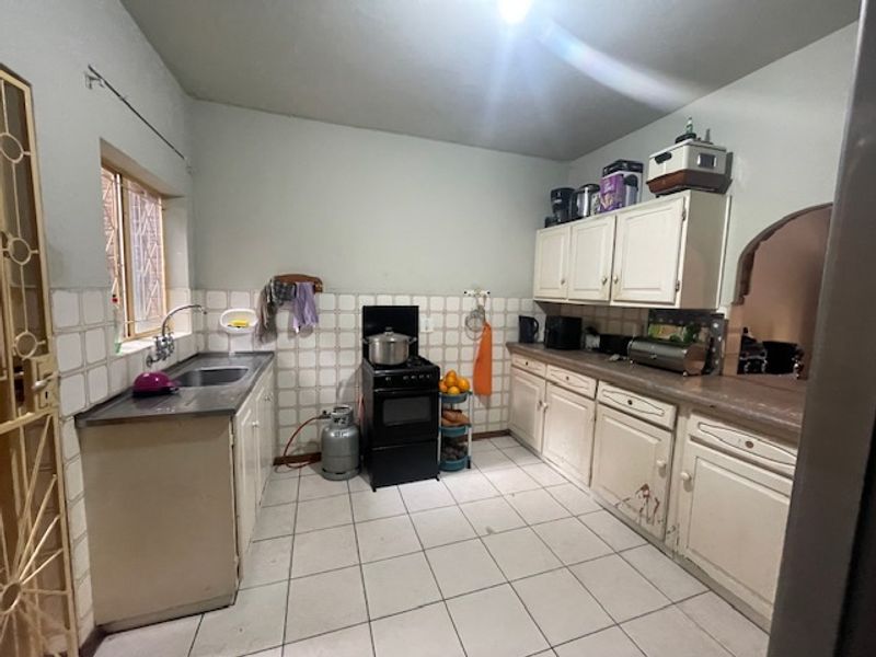 A functional kitchen featuring tiled flooring, a tiled backsplash, built-in cabinetry, and a freestanding stove.