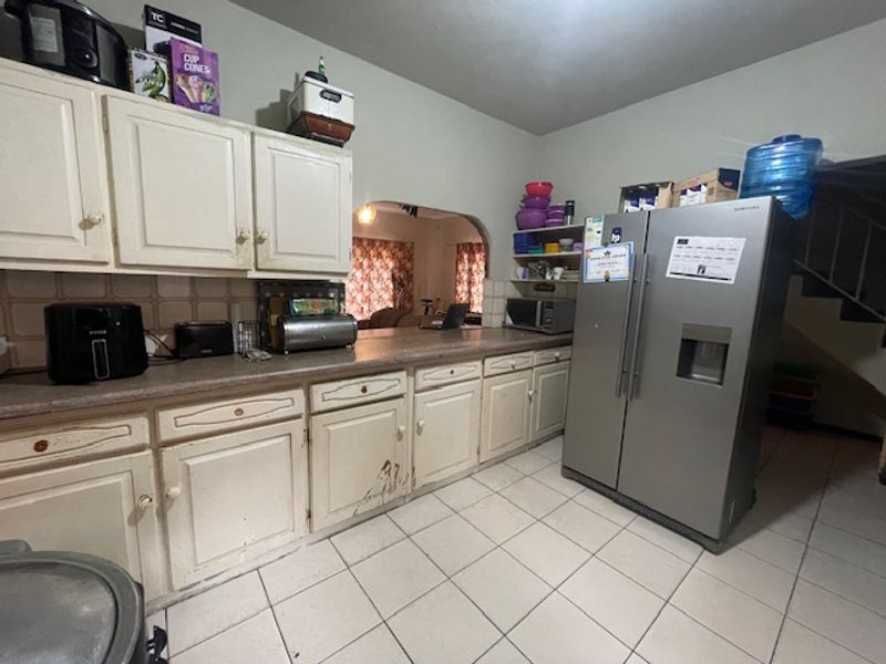 A functional kitchen featuring tiled flooring, laminate countertops, and traditional built-in cabinetry with an open archway leading to the adjacent living area.
