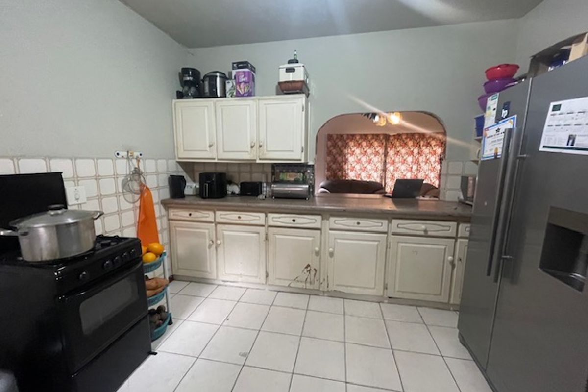 A functional kitchen featuring tiled flooring, a tiled splashback, and built-in cabinetry with a laminate countertop, connected to the living area via an archway.