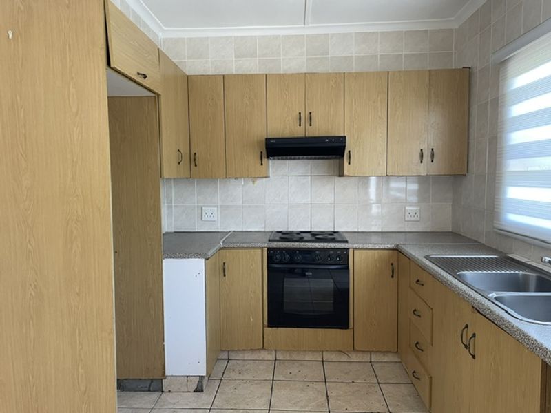 A dated kitchen featuring laminate cabinetry, built-in oven with hob, extractor fan, and a double stainless steel sink with tiled splashbacks.