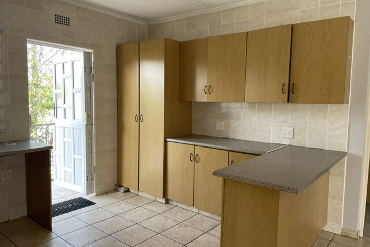 A functional kitchen featuring laminate cabinetry, tiled walls and flooring, and a breakfast bar, with direct access to an outdoor area.