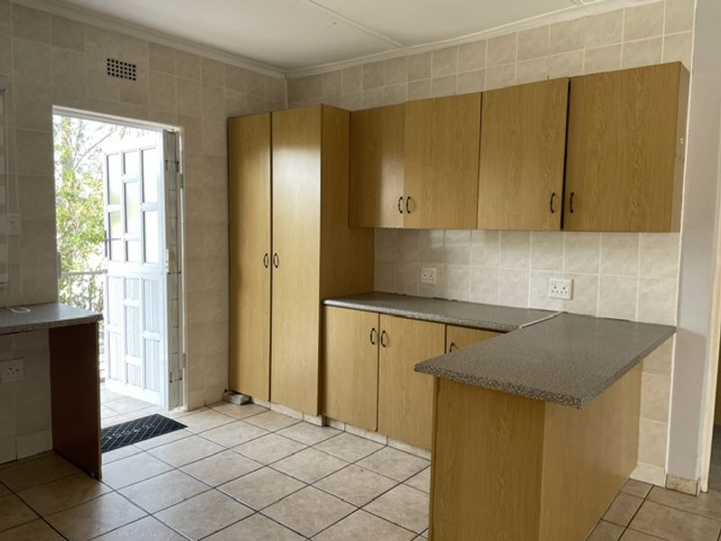 A functional kitchen featuring laminate cabinetry, tiled walls and flooring, and a breakfast bar, with direct access to an outdoor area.