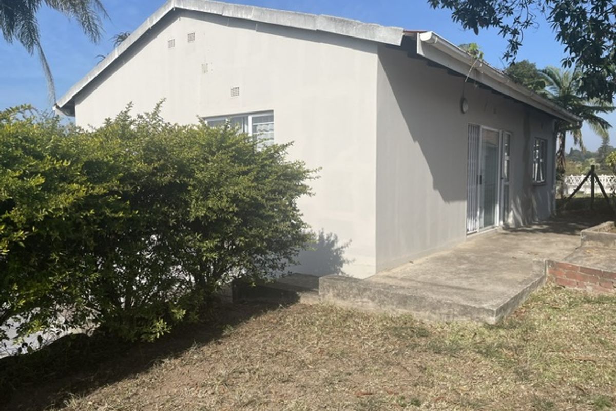 Rear view of the cottage featuring a concrete patio, sliding glass door with security gate, and a small brick retaining wall in the garden.