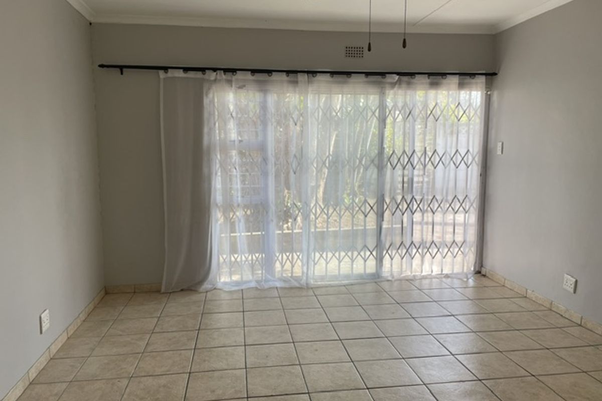 An empty living room featuring neutral tiled flooring, a ceiling fan, and a sliding glass door with an integrated security gate leading outdoors.