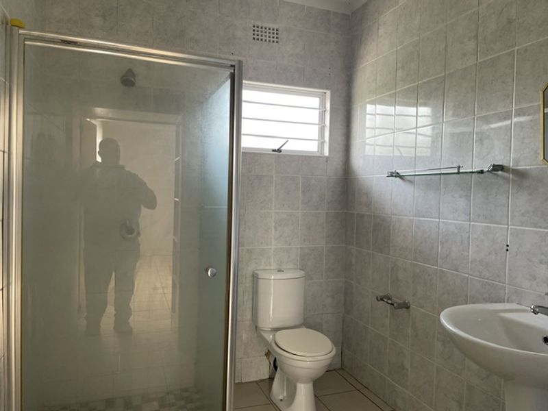A functional bathroom featuring a shower enclosure, pedestal basin, and toilet, finished with neutral wall and floor tiling.