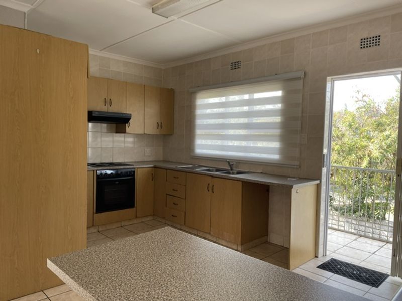 A functional kitchen featuring built-in wooden cabinetry, laminate countertops, an integrated oven and hob, and direct access to an outdoor patio area.