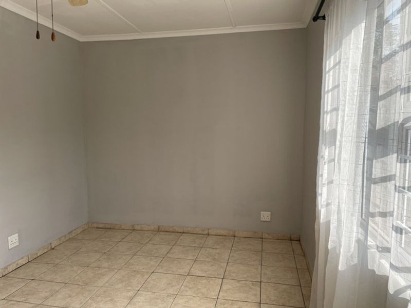 A clean, empty bedroom featuring neutral grey walls, tiled flooring, and a ceiling fan, offering a blank canvas for personalization.