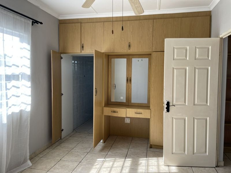 A bedroom featuring built-in wooden cupboards with an integrated vanity, tiled flooring, and a ceiling fan.