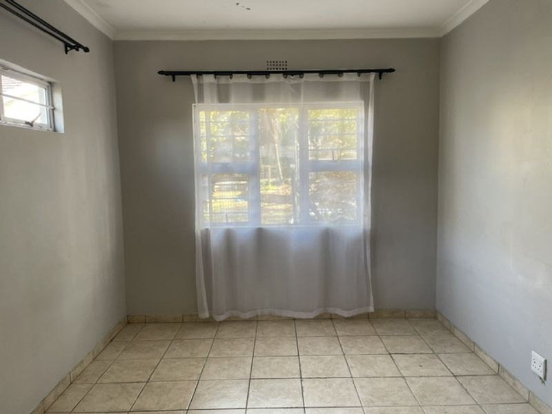 An empty bedroom featuring tiled flooring, security bars on the windows, and neutral wall paint, offering a blank canvas for potential updates.