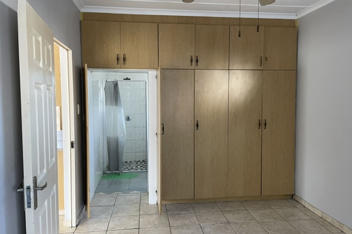 A bedroom featuring extensive built-in wooden cupboards, tiled flooring, and a ceiling fan, with direct access to an en-suite bathroom.