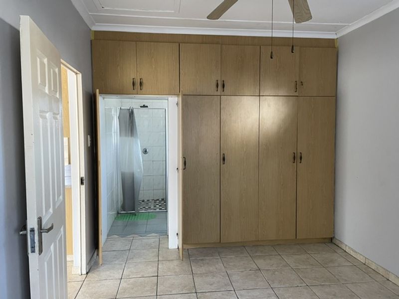 A bedroom featuring extensive built-in wooden cupboards, tiled flooring, and a ceiling fan, with direct access to an en-suite bathroom.