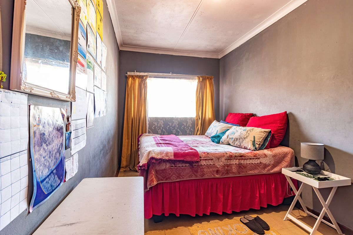 A compact bedroom featuring grey walls and a window with curtains. The room requires cosmetic updates to the ceiling and wall finishes.