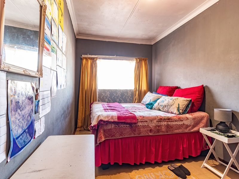 A compact bedroom featuring grey walls and a window with curtains. The room requires cosmetic updates to the ceiling and wall finishes.