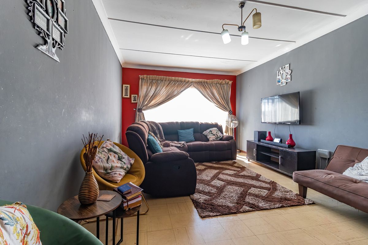 A living room featuring tiled flooring and a ceiling fan, with a red accent wall and neutral grey walls.
