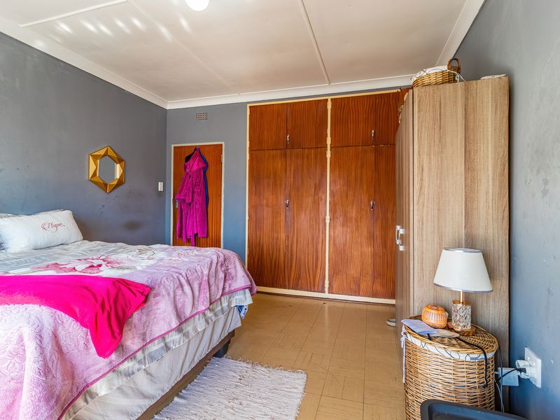 A bedroom featuring built-in wooden cupboards, tiled flooring, and grey painted walls, offering a functional space with potential for cosmetic updates.
