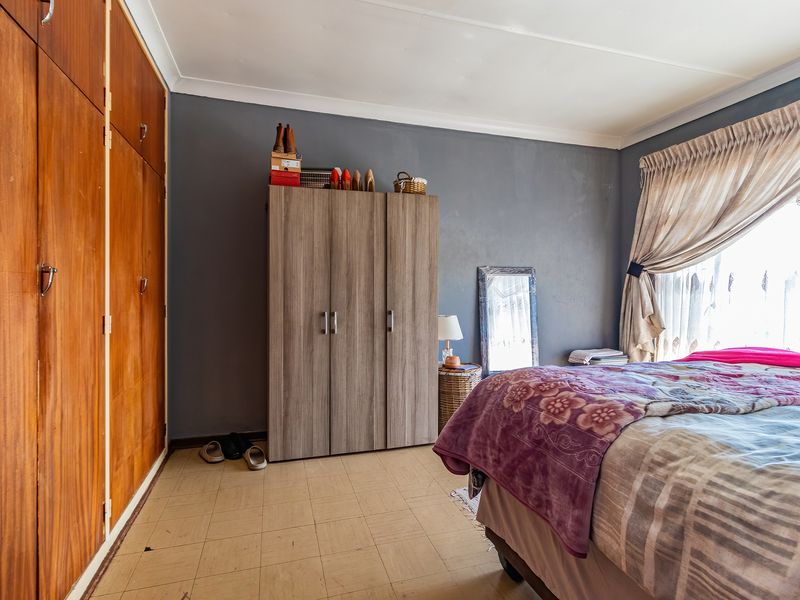 A bedroom featuring built-in wooden cupboards, tiled flooring, and natural light through a window with curtain rails.