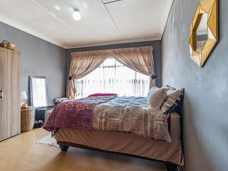 A bedroom featuring tiled flooring and grey painted walls, providing a functional space with natural light through the window.