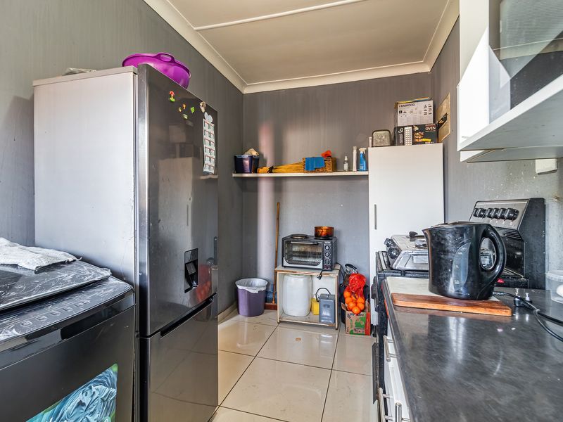 A compact kitchen area featuring tiled flooring, laminate countertops, and built-in shelving, requiring some cosmetic updates to the wall finishes.