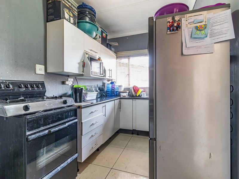 A compact kitchen featuring built-in cabinetry, laminate countertops, a freestanding stove, and tiled flooring, requiring cosmetic updates to improve its overall condition.