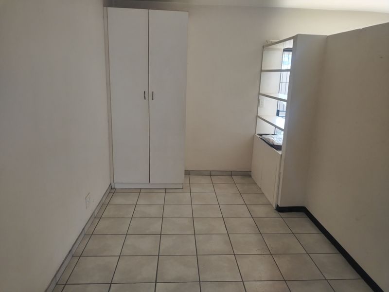 An empty bedroom featuring ceramic floor tiles, a built-in wardrobe, and a built-in shelving unit, offering a blank canvas for personalization.