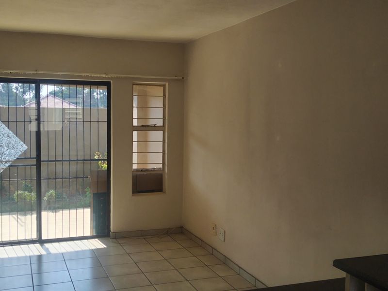 An open-plan living area featuring tiled flooring, built-in cabinetry, and a sliding glass door with security gate leading to the exterior.