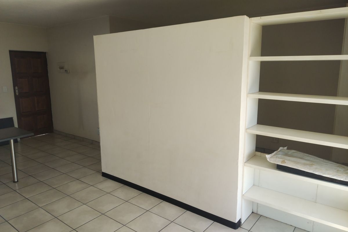 An empty living area featuring tiled flooring, a central partition wall, and built-in shelving, offering a blank canvas for interior design.