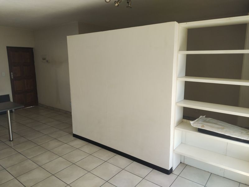 An empty living area featuring tiled flooring, a central partition wall, and built-in shelving, offering a blank canvas for interior design.