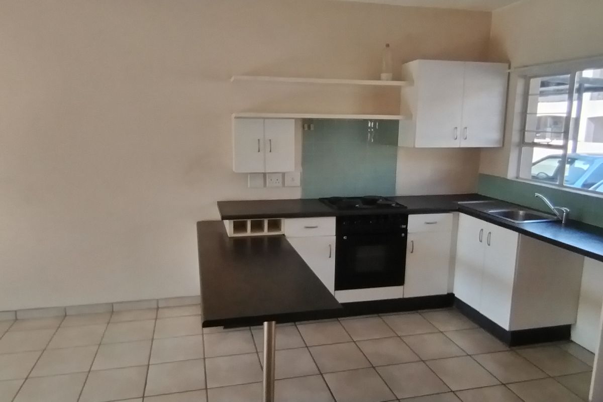 A functional kitchen featuring white cabinetry, dark laminate countertops, a built-in oven, hob, and a breakfast bar, finished with tiled flooring.