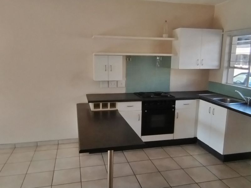 A functional kitchen featuring white cabinetry, dark laminate countertops, a built-in oven, hob, and a breakfast bar, finished with tiled flooring.