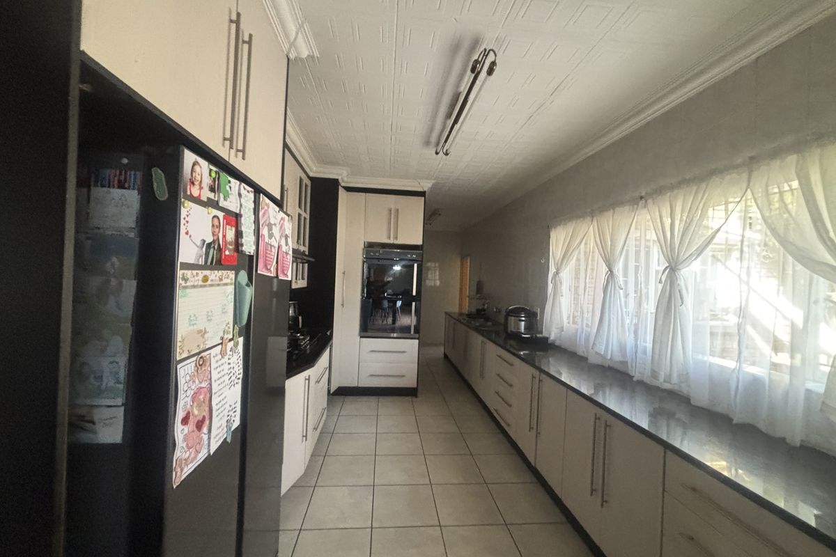A long galley-style kitchen featuring extensive built-in cabinetry, granite countertops, a built-in oven, and tiled flooring with a decorative ceiling finish.