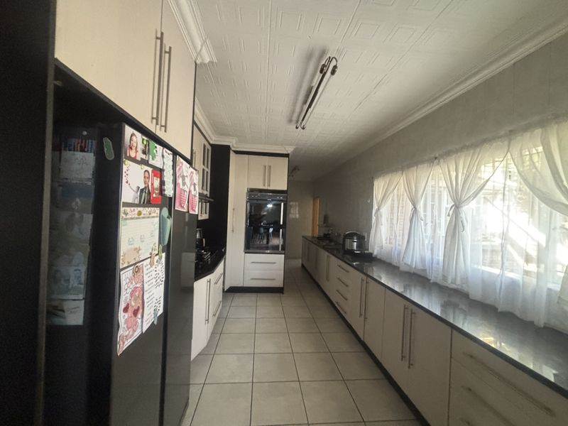 A long galley-style kitchen featuring extensive built-in cabinetry, granite countertops, a built-in oven, and tiled flooring with a decorative ceiling finish.